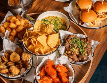 Platter of game day food with sliders, wings, fries, and appetizers at National The Well in Toronto