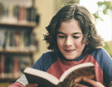 Woman smiling while reading a book in a cozy bookstore setting.