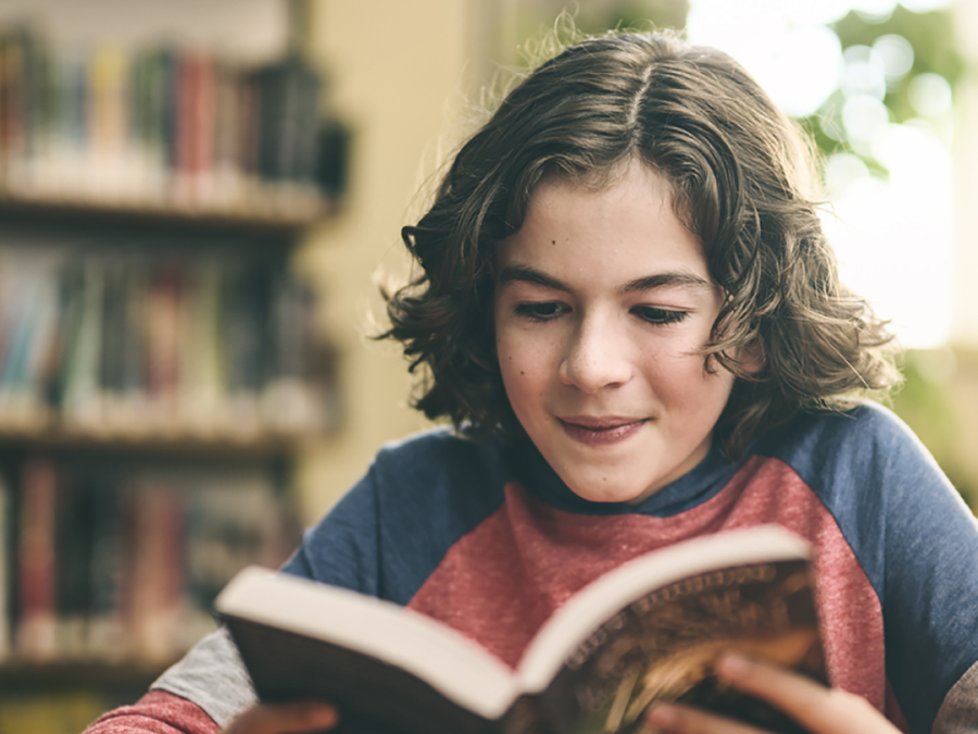 Woman smiling while reading a book in a cozy bookstore setting.